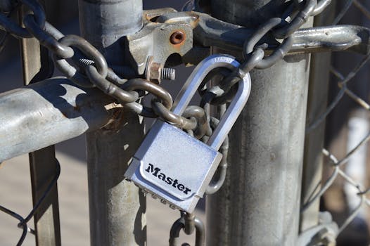 Detailed view of a padlock securing a metal gate with a chain, emphasizing safety and security.